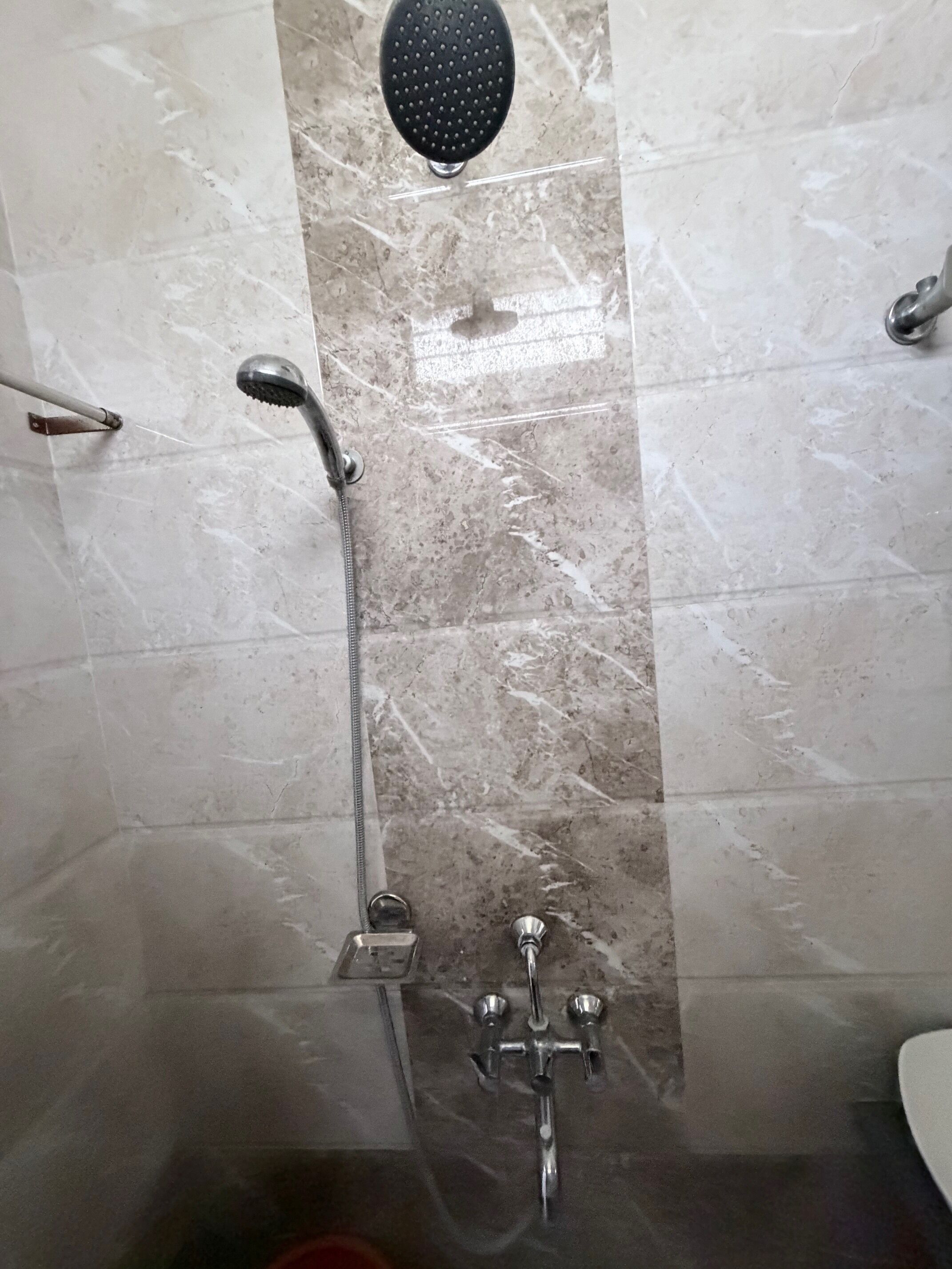 A bathroom with a shower, a handheld showerhead, and a wall-mounted faucet.