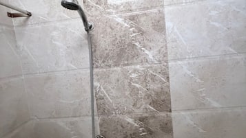 A bathroom with a shower, a handheld showerhead, and a wall-mounted faucet.