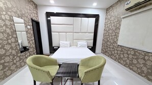 A hotel room with a bed, two chairs, a small table, a mirror, and an air conditioning unit. - Hotel SR Executive Akola (Akola)