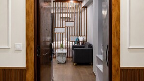 A hallway leading to a room with a bed, a sofa, and a small table with a plant. - Xenious Smart Suites Greater Noida (Greater Noida)