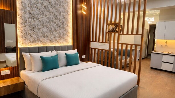 A modern bedroom with a large bed, a ceiling fan, and a decorative wall panel. - Xenious Smart Suites Greater Noida (Greater Noida)