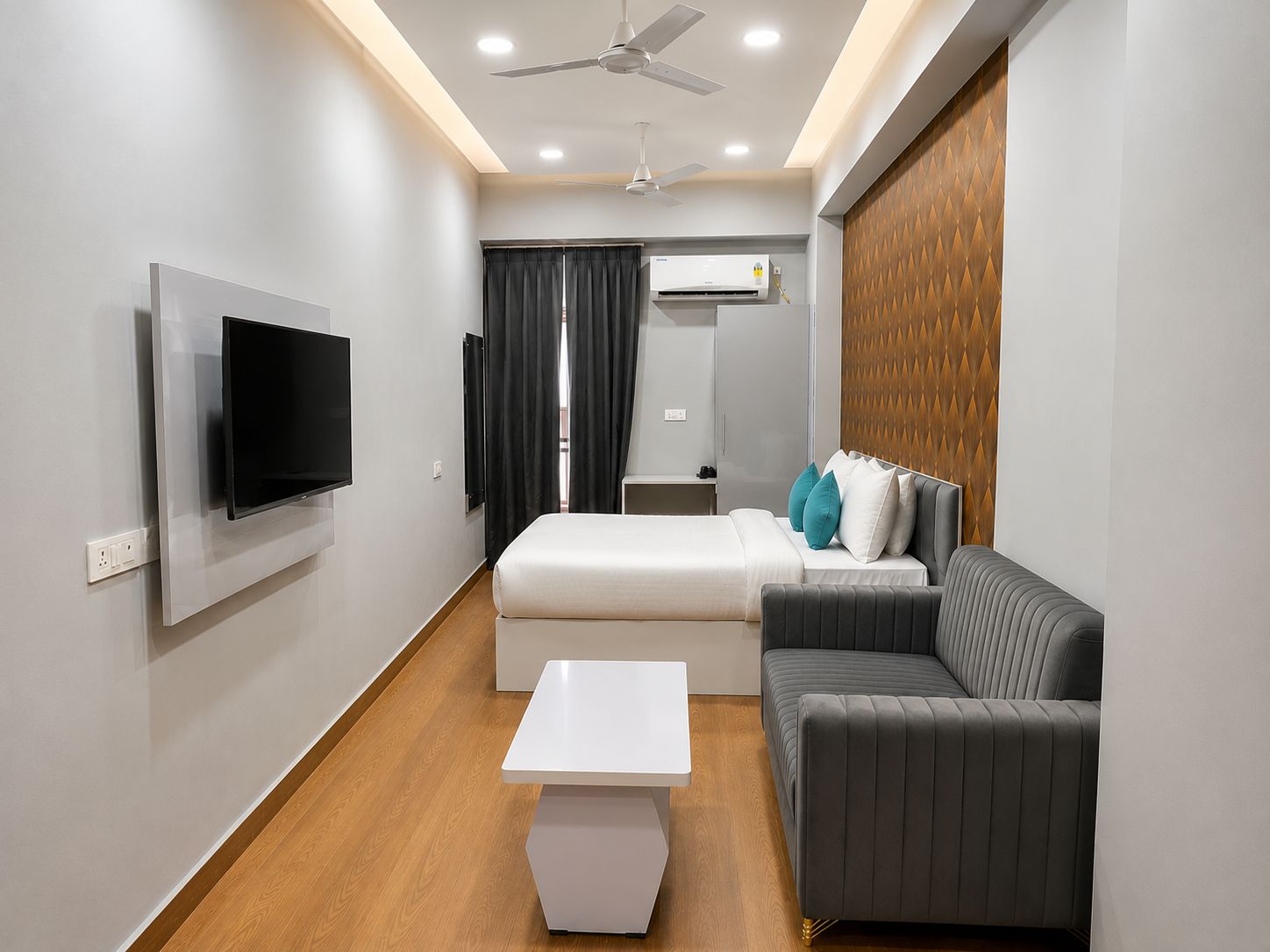 A modern hotel room with a flat-screen TV, a bed, a sofa, a small table, and a ceiling fan.