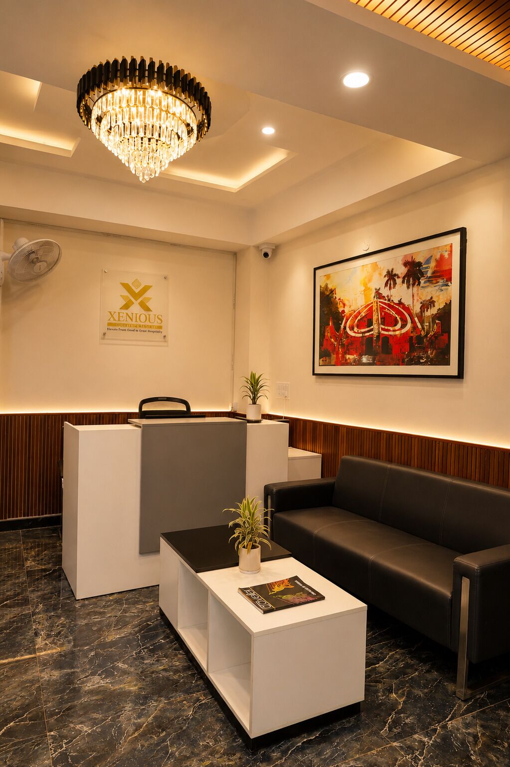 A reception area with a chandelier, a reception desk, a couch, a coffee table, a plant, and a framed artwork on the wall.