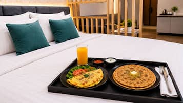 Cama bem arrumada com bandeja de café da manhã, incluindo uma omelete, pão achatado e um copo de suco de laranja.