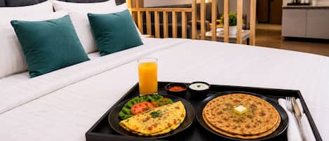 A neatly made bed with a tray of breakfast including an omelette, a flatbread, and a glass of orange juice.