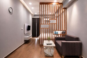 A modern living room with a sofa, coffee table, TV, and a decorative wooden partition. - Xenious Smart Suites Greater Noida (Greater Noida)