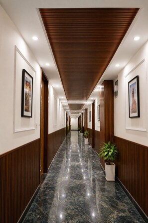 A long, well-lit hallway with wooden paneling, marble flooring, and framed pictures on the walls. - Xenious Smart Suites Greater Noida (Greater Noida)