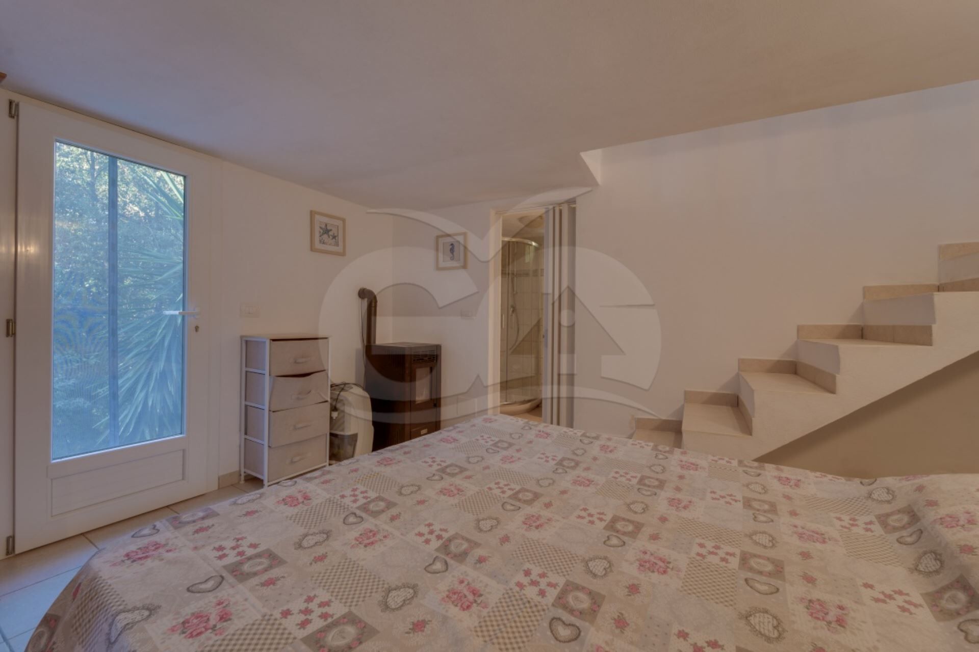 A bedroom with a bed, a dresser, a shower, and a staircase.