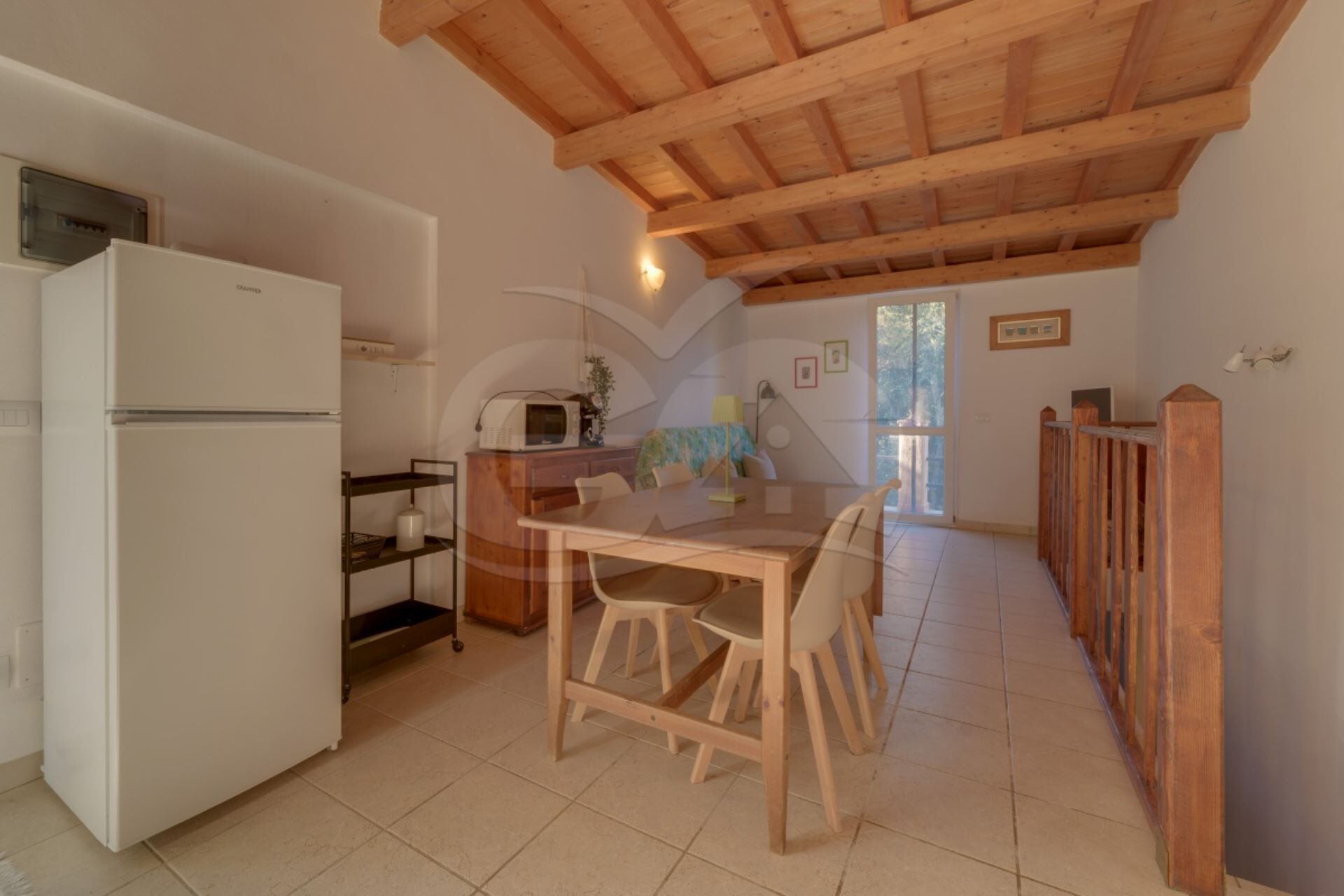 Une cuisine avec un réfrigérateur blanc, un plafond en bois et un coin repas comprenant une table et des chaises.