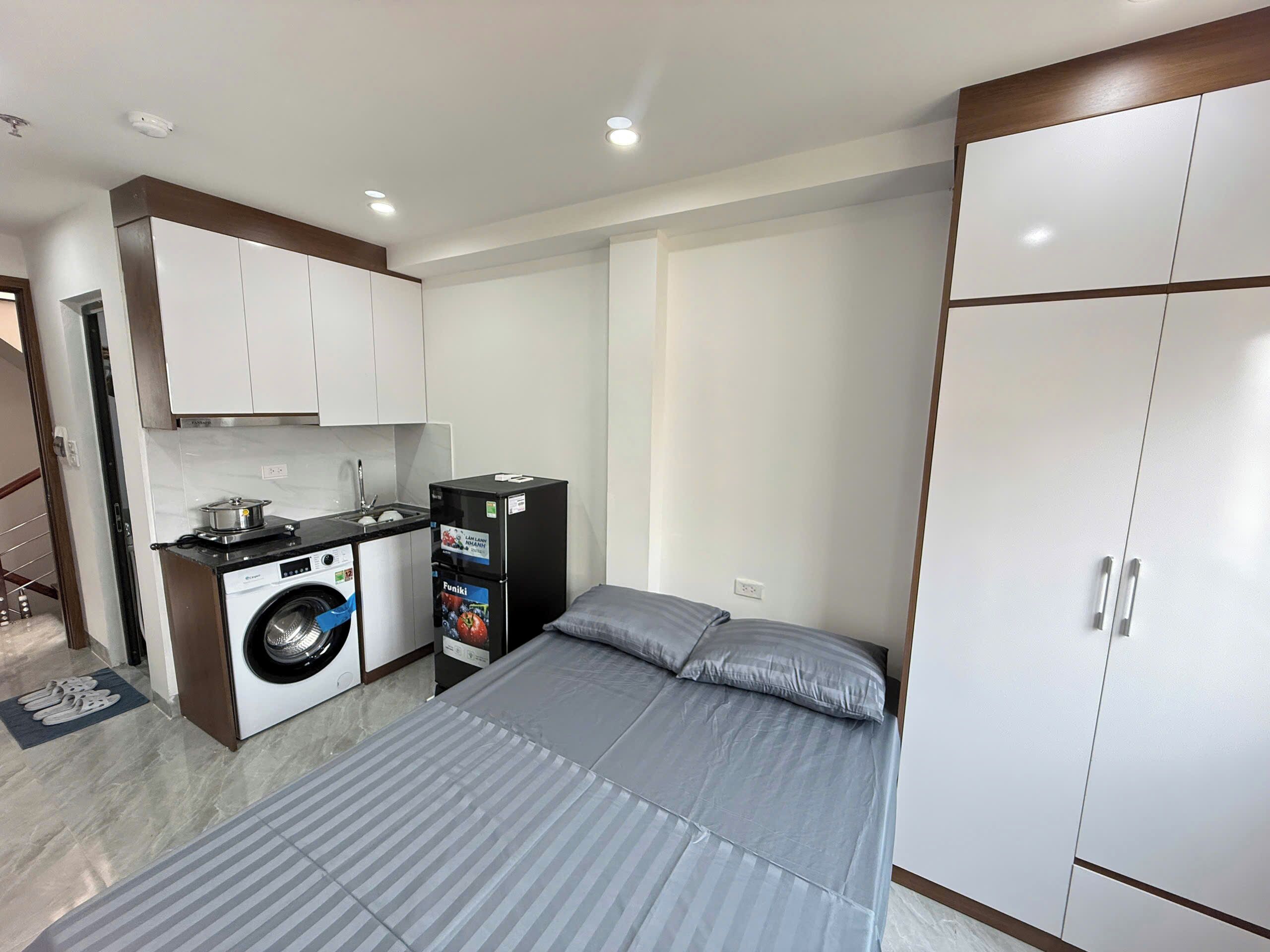 A compact hotel room with a bed, a wardrobe, a washing machine, and a small kitchenette.