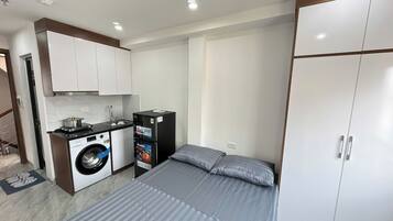 A compact hotel room with a bed, a wardrobe, a washing machine, and a small kitchenette.