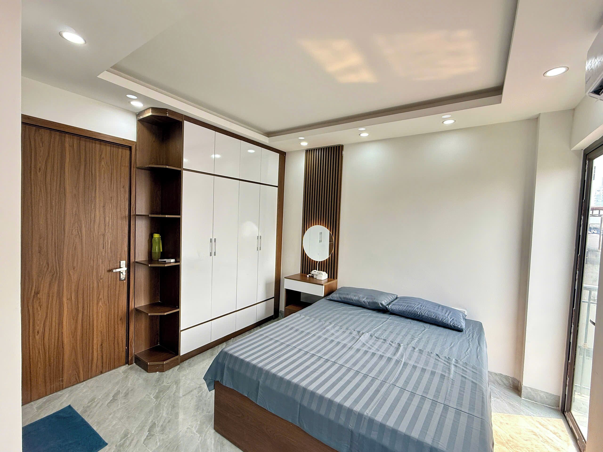 A bedroom with a bed, wardrobe, vanity, and a window.