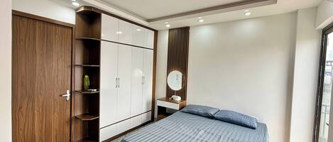 A bedroom with a bed, wardrobe, vanity, and a window.