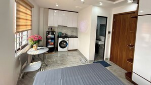 A compact kitchen with a washing machine, a dining area with a table and chairs, and a large bed. - Era Apartment Hoang Hoa Tham (Hanoi)