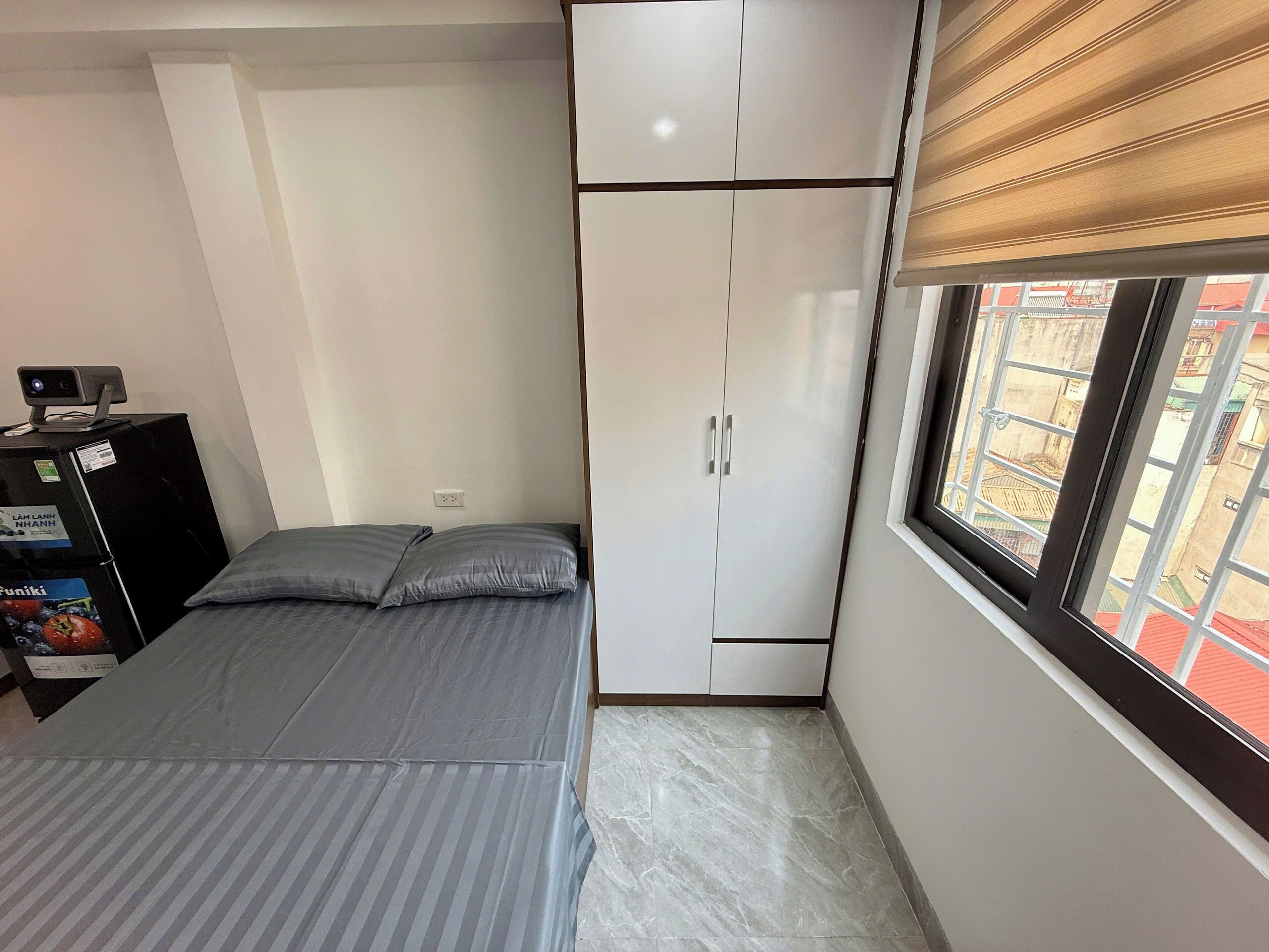 A bedroom with a bed, a wardrobe, a desk with a computer, and a window with a view.
