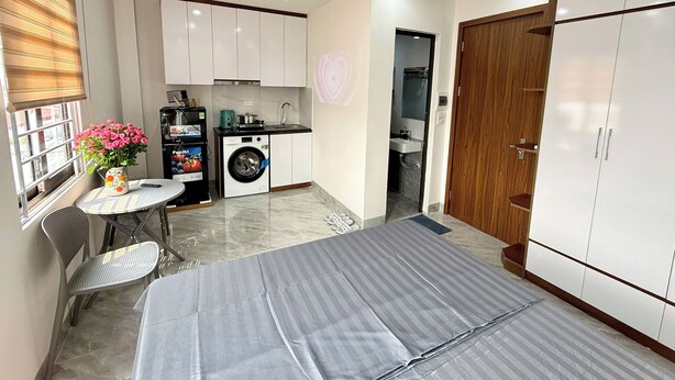 A compact living space with a kitchen, a washing machine, a dining area with a table and chairs, and a wardrobe. - Era Apartment Hoang Hoa Tham (Hanoi)