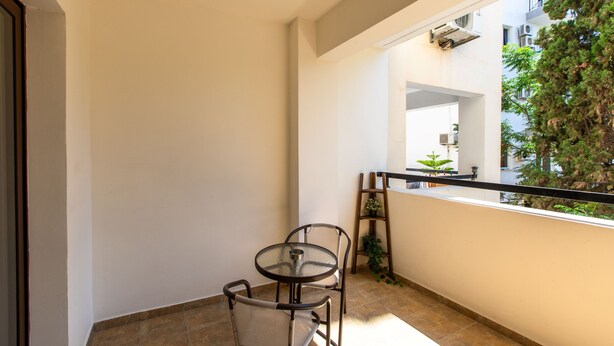 Een balkon met een glazen tafel en stoelen, een ladder en uitzicht op een gebouw en bomen.
