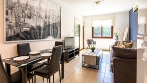 Een moderne woonkamer met een eethoek, een groot stadsgezicht schilderij, een televisie en een bank.