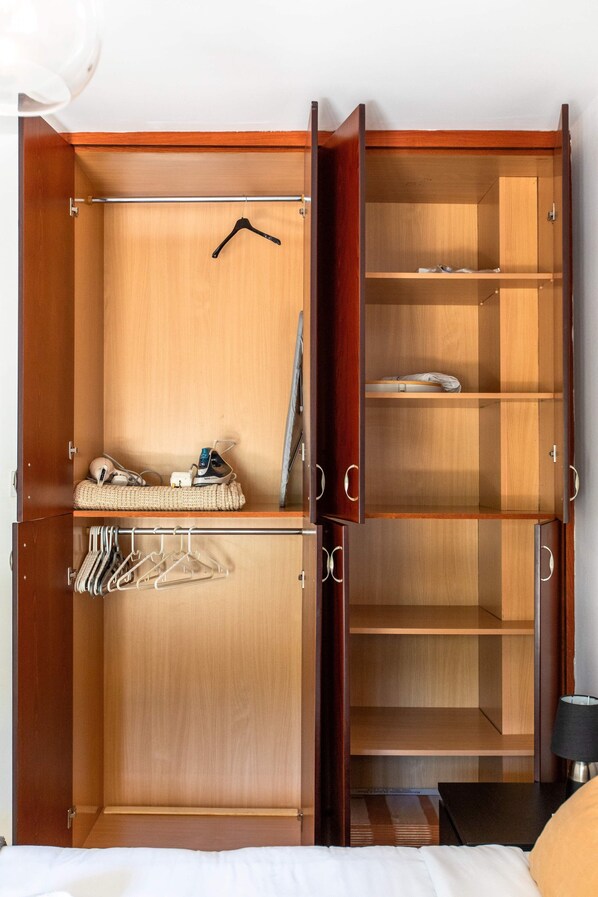 A wooden wardrobe with multiple compartments, a hanging rack, and a small shelf with a folded towel. - Mia 1-BR Apartment & Balcony in Larnaca (Larnaca)