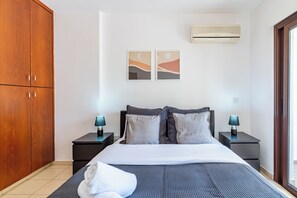 A bedroom with a bed, two bedside tables, a wooden wardrobe, an air conditioning unit, and two wall-mounted artworks. - Mia 1-BR Apartment & Balcony in Larnaca (Larnaca)