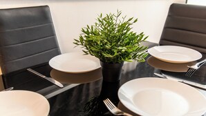 Een eettafel met een potplant, witte borden en bestek.