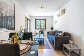 A modern living room with a sofa, dining table, chairs, and a large window. - Mia 1-BR Apartment & Balcony in Larnaca (Larnaca)
