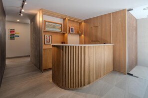 Ein Empfangsschalter mit Holzoptik, ein an der Wand befestigtes Schild in verschiedenen Farben und ein gerahmtes Bild.