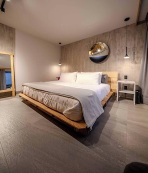 Ein modernes Schlafzimmer mit einem großen Bett, einem Holzkopfteil, einem Nachttisch und einem wandmontierten Spiegel.