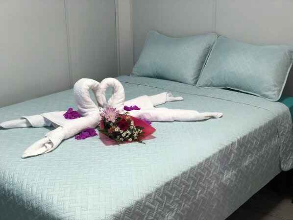 Un lit avec une couette bleu clair, deux oreillers et un bouquet de fleurs.