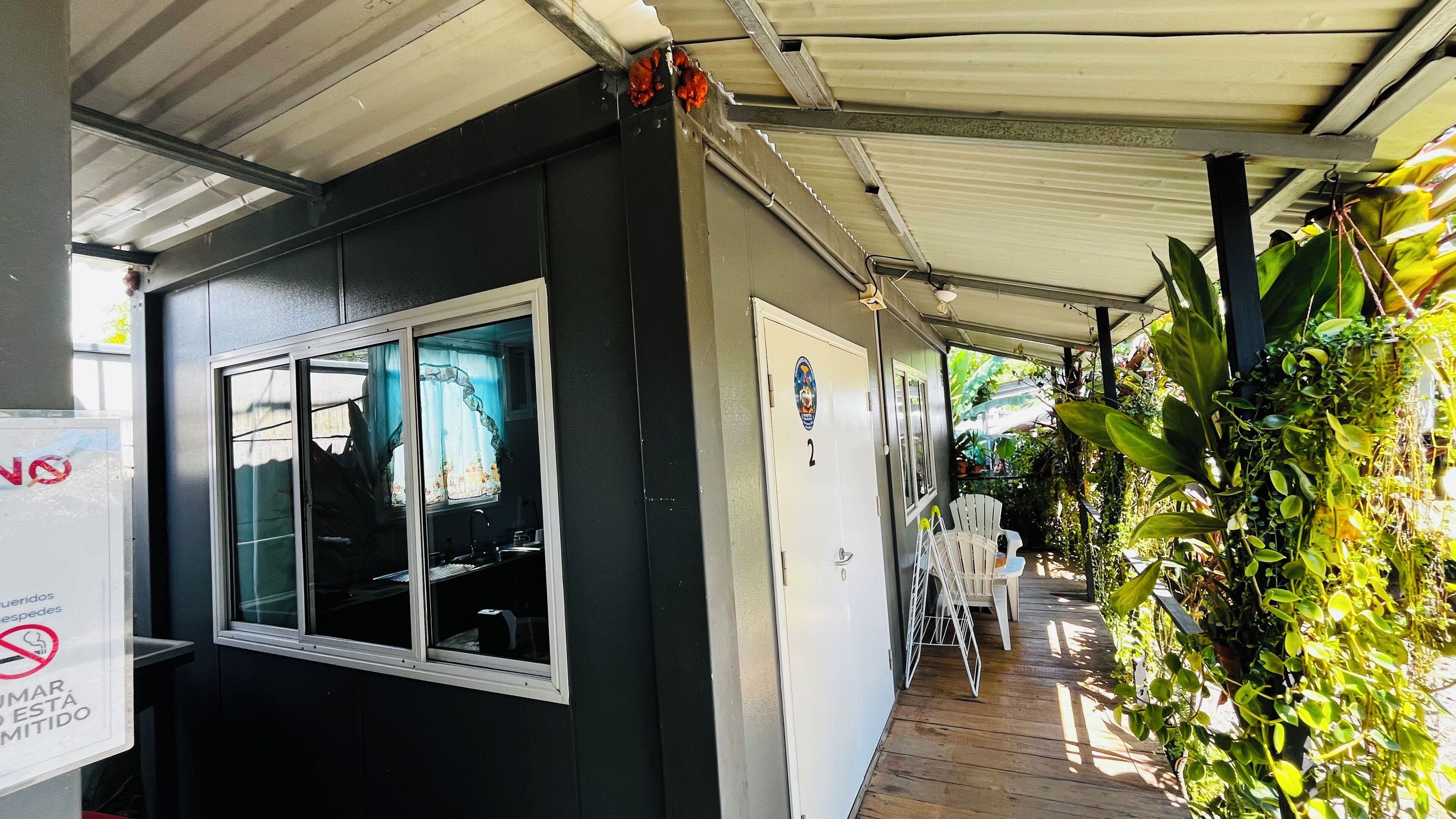 A covered outdoor area with a window, a door, and a sign indicating no smoking.
