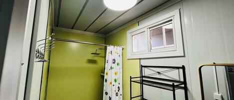 Une salle de bain avec une douche, une fenêtre et une étagère en métal.