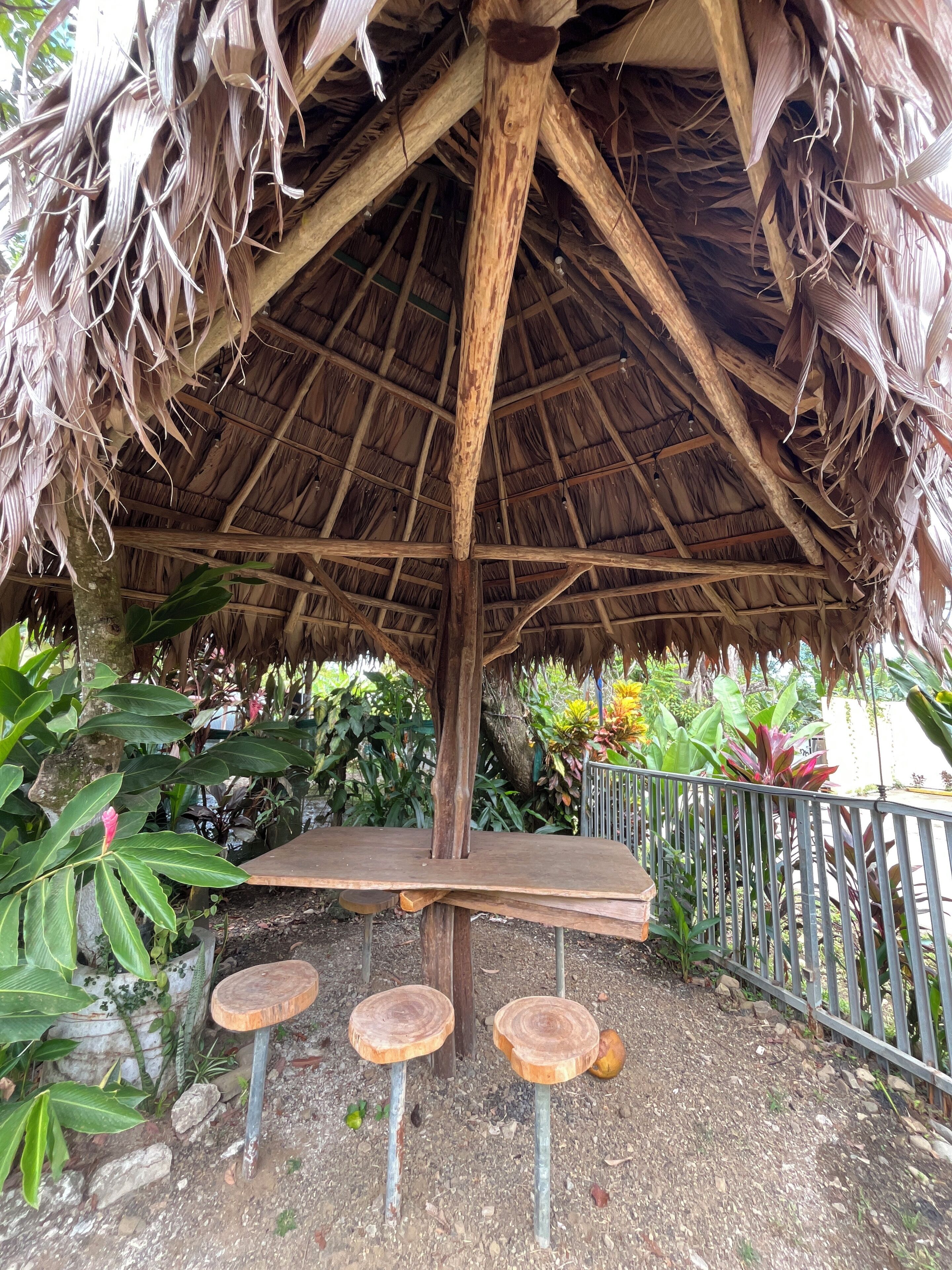 A thatched-roof structure with a central wooden platform and two stools.