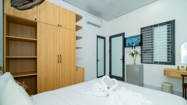 A hotel room with a bed, a wooden wardrobe, a television, a plant, and a window with blinds. - Green Homestay  (Da Nang)