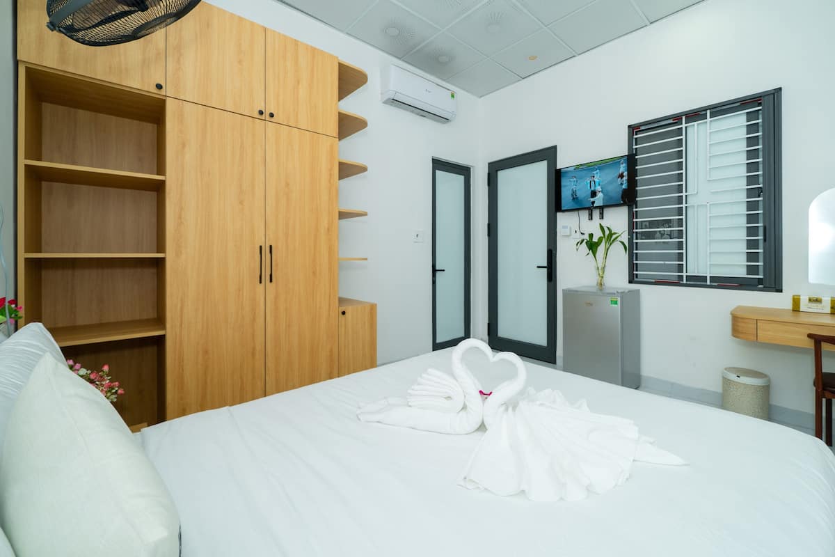 Ein Hotelzimmer mit einem Bett, einem Holzschrank, einem Fernseher, einer Pflanze und einem Fenster mit Jalousien.