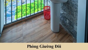 A balcony with a sink, a red basket, and a view of greenery and buildings. - Green Homestay  (Da Nang)