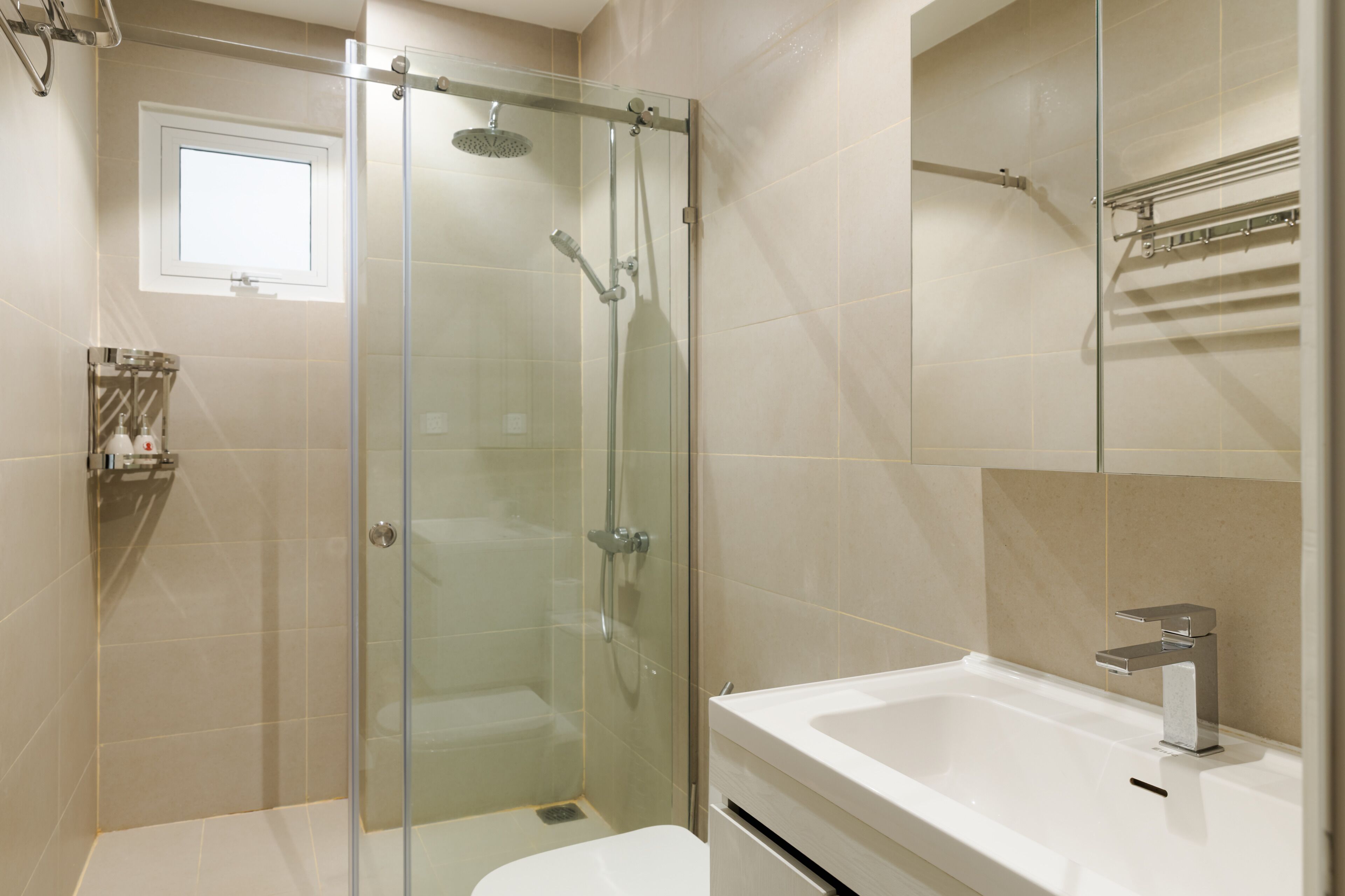 A modern bathroom with a glass-enclosed shower, a white bathtub, and a small window above the shower.