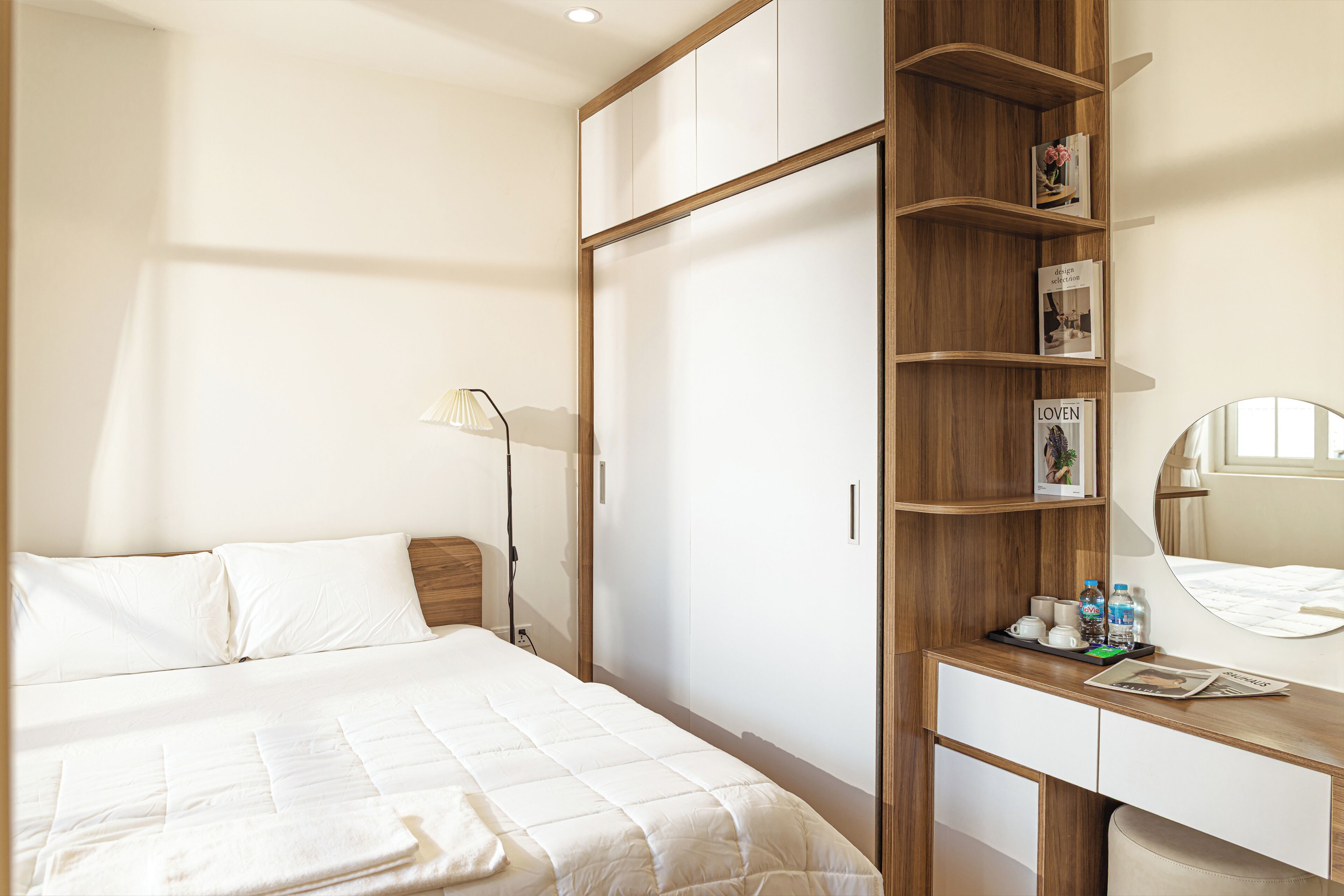 Ein Hotelzimmer mit einem Bett, einem Schreibtisch mit Spiegel, einem Bücherregal und einem Kleiderschrank.