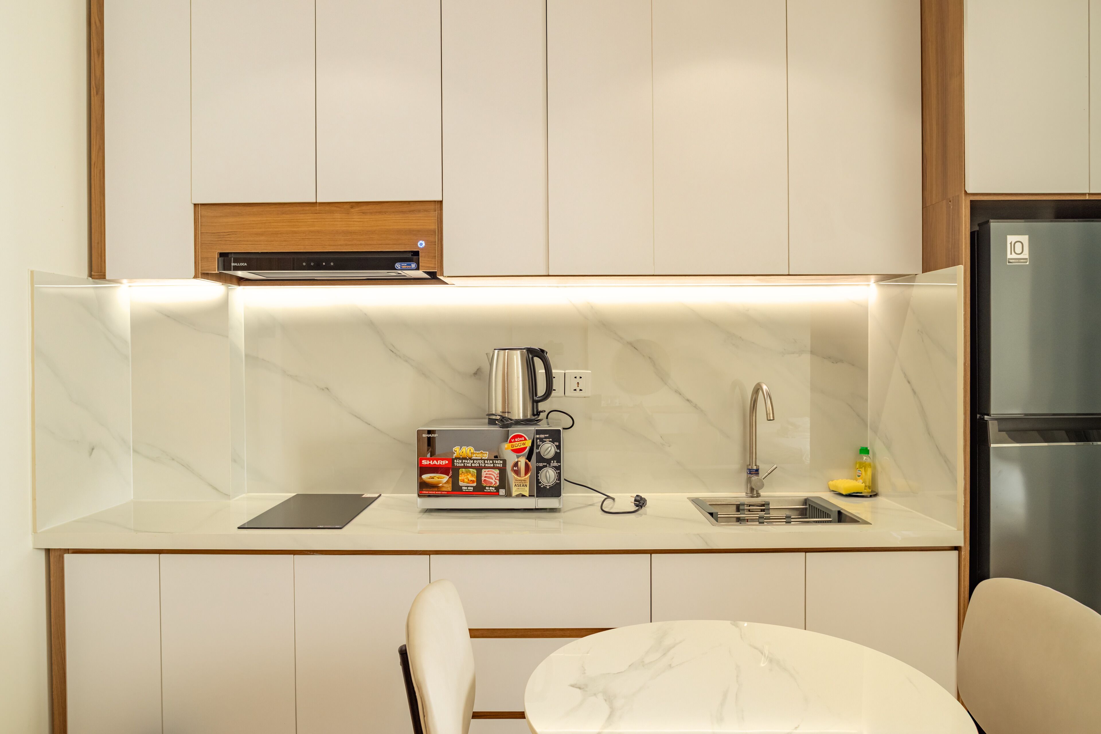 A modern kitchen with a marble countertop, a built-in coffee maker, a sink, and a refrigerator.