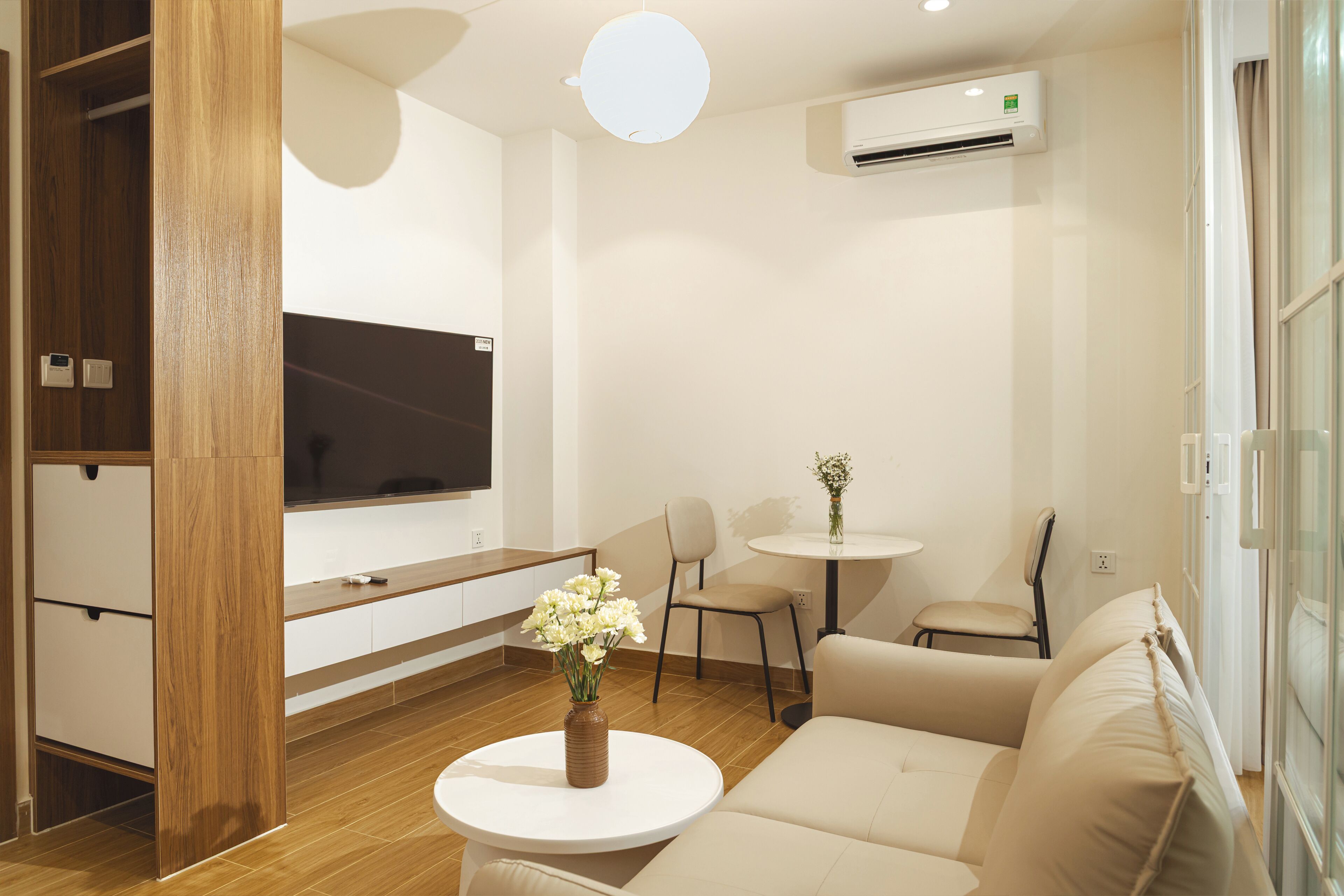 Una sala de estar moderna con un sofá, una mesa de centro con flores, un televisor y una pequeña mesa con sillas.