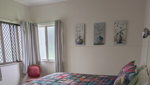 A bedroom with a bed, a window with curtains, a chair, and wall art.