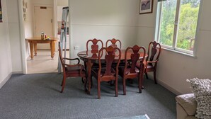 A dining area with a round wooden table and chairs, a window with a view of trees, and a door leading to another room.