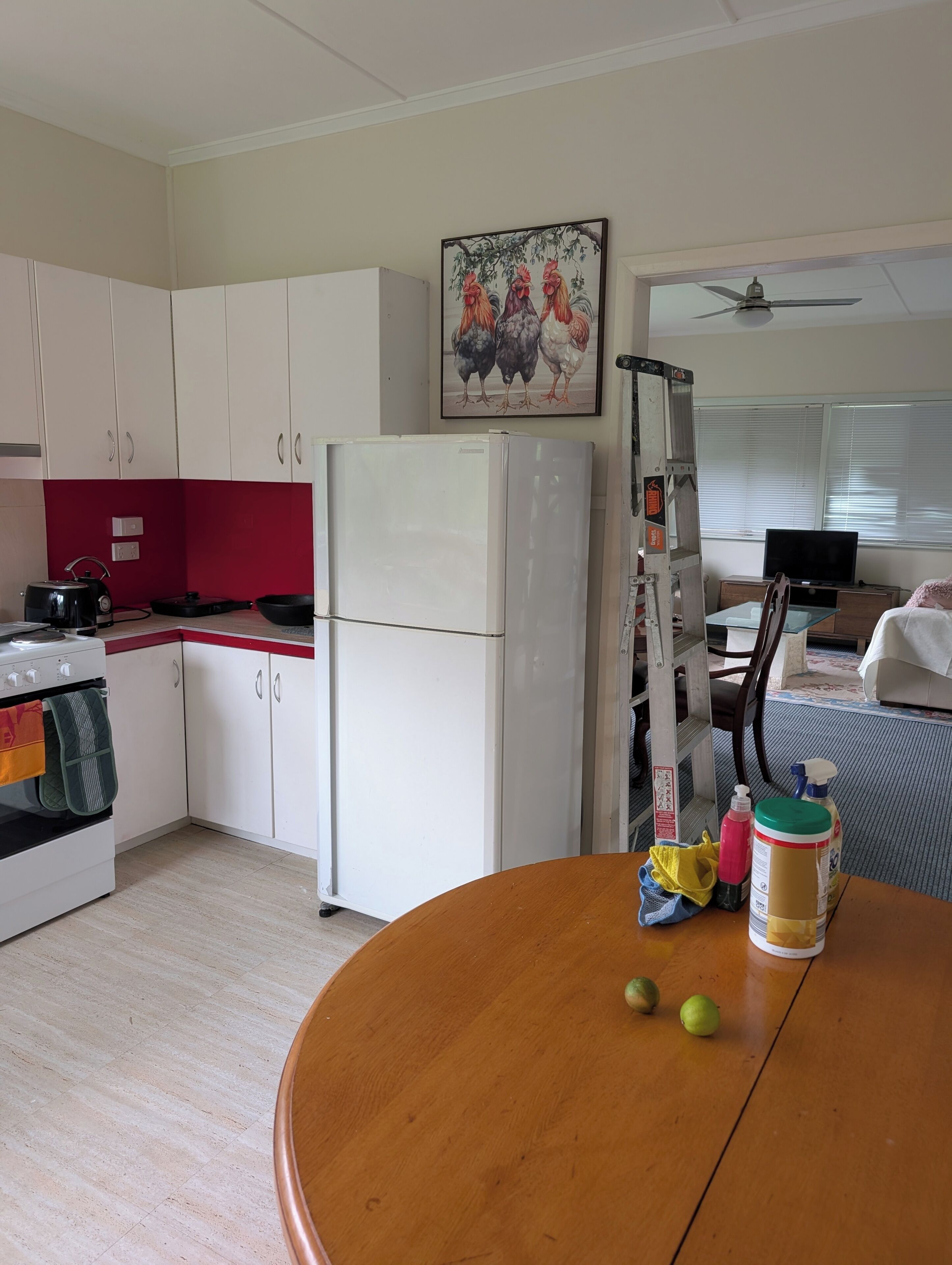 A kitchen with white cabinets, a refrigerator, a stove, and a painting of roosters on the wall.