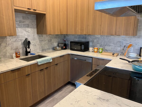A modern kitchen with wooden cabinets, a marble backsplash, a built-in dishwasher, a microwave, and a sink.