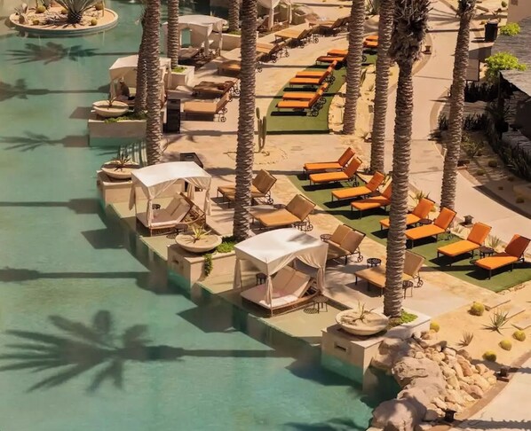 Área de piscina en un resort con sillas de descanso y sombrillas, rodeada de palmeras.