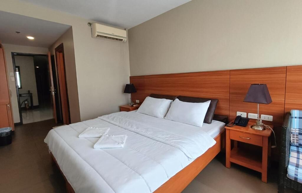 Habitación de hotel con una cama grande, dos mesitas de noche, un ventilador de aire acondicionado y vistas al pasillo.