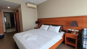 Habitación de hotel con una cama grande, dos mesitas de noche, un ventilador de aire acondicionado y vistas al pasillo.