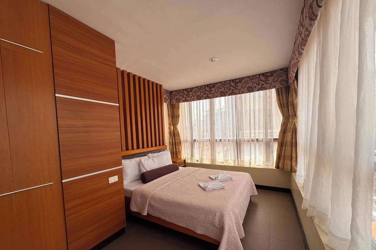 Un dormitorio con cama, armario de madera y ventana con cortinas.