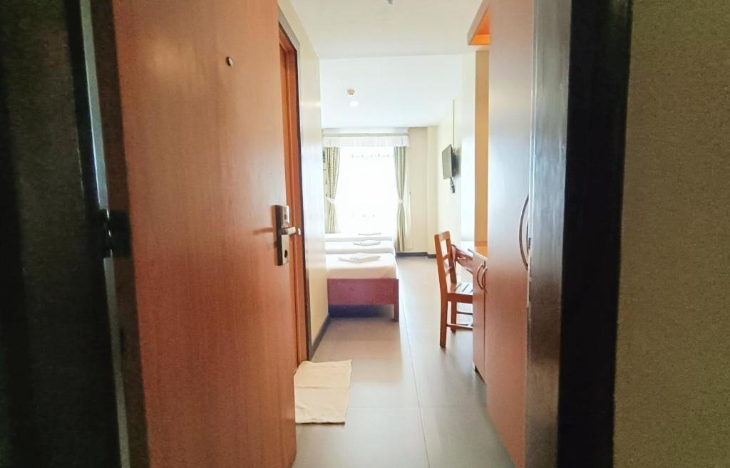 Un pasillo que da a una habitación con cama, una silla y una mesita.