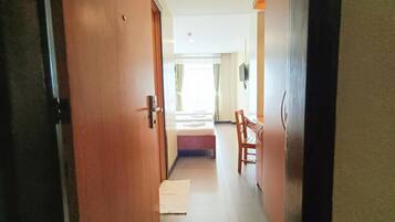Un pasillo que da a una habitación con cama, una silla y una mesita.
