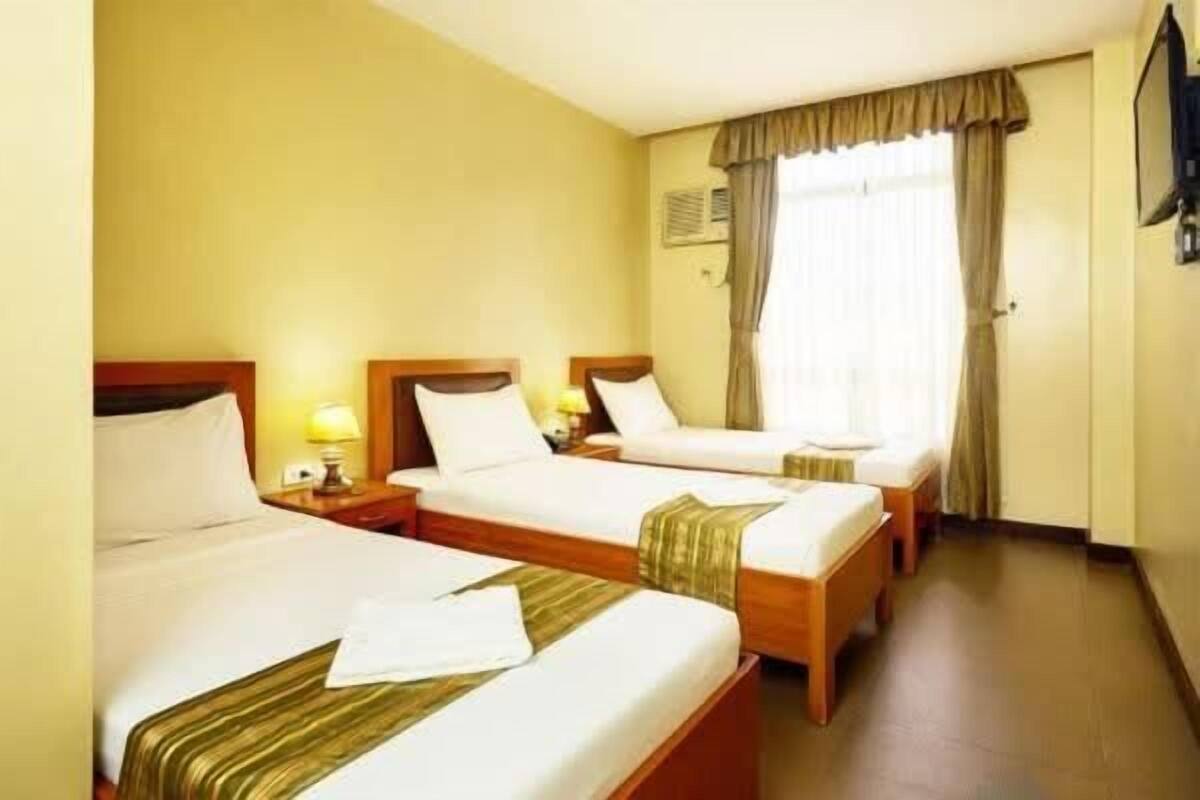 Habitación de hotel con dos camas individuales, televisión y ventana con cortinas.
